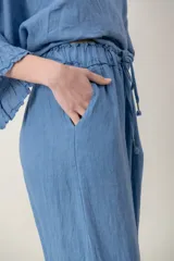 Pantalon de lino color azul, de corte ancho y relajado, con cintura elastizada ajustable mediante cordón y bolsillos laterales. Presenta detalles de alforzas en los bajos.