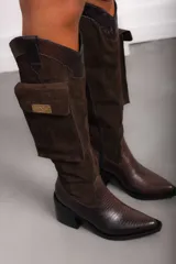 Bota alta de cuero marrón, con taco cuadrado y punta fina. Cuenta con un bolsillo lateral incorporado con solapa y placa metálica con logo.