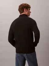 Sweater de punto fino de lana merino, con cuello alto y cierre de media apertura. Presenta mangas largas con puños acanalados y logo de la marca bordado en el pecho.