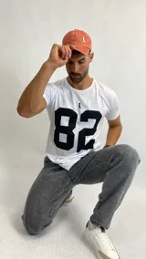 Remera blanca de manga corta con estampado frontal del número 82 en color negro y un pequeño logo de un pingüino con galera.