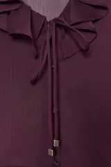 Blusa de color bordó con escote en V profundo adornado con volantes, mangas largas con puños y detalle de peplum en el ruedo. Cuenta con cierre frontal de botones forrados en la misma tela.