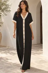 Vestido largo negro de corte holgado, con cuello en V y listón frontal en color beige contrastante. Cuenta con botones frontales y mangas cortas con vuelta en el mismo tono beige.