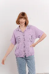 Camisa lila de tela arrugada, con cuello clásico y solapas a rayas. Tiene dos bolsillos delanteros con pespuntes a rayas y base levemente elastizada. Cierre frontal con botones.