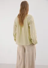 Blusa verde claro de manga larga con detalles de puntilla en el escote en V y en los hombros, corte holgado.