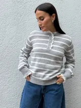 Sweater de punto a rayas horizontales grises y blancas, con cuello redondo, cierre frontal parcial con botones y delicados detalles de puntilla en el cuello y los puños.