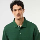 Remera polo de piqué de algodón color verde oscuro, de manga corta, con cuello camisero y cartera de tres botones. Presenta una textura sutil de líneas horizontales en relieve y una pequeña etiqueta decorativa en el borde inferior.