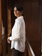 Camisa blanca de corte holgado con cuello camisero y mangas largas que presentan un diseño bordado en relieve con motivos orgánicos en tono beige.