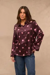 Camisa de satén color bordó con estampado de lunares rosados, cuello camisero, cierre frontal con botones y mangas largas con puños anchos.