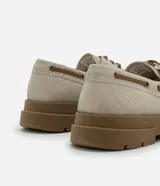 Zapato estilo dockside de color beige claro, confeccionado en gamuza sintética, con cordones marrones y suela track gruesa de goma color marrón. Presenta costuras visibles en la puntera y ojales metálicos para los cordones.