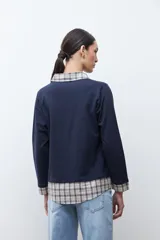 Sweatshirt azul marino de manga larga con cuello en V, superpuesto a una camisa de cuadros beige y azul que asoma en el cuello, puños y ruedo.