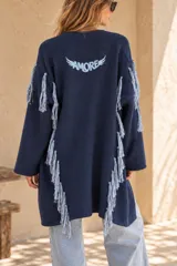 Saco tejido de punto azul marino, de corte largo y relajado, con flecos colgantes en las mangas y laterales, y un bordado en la espalda con la palabra "AMORE" y alas.