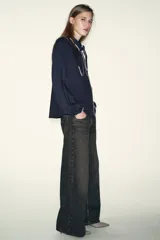 Blusa de manga larga en color azul marino, con cuello solapa y lazo frontal. Presenta detalles de pespuntes bordados en color crema a lo largo del cuello, lazo, cierre frontal y puños. Cierre frontal con botones.