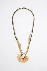 Collar doble con cadena dorada y cordón negro, con colgante en forma de flor de rafia y centro de cerámica blanca con detalles en negro.