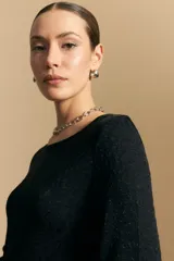 Top negro de manga larga acampanada con escote pronunciado en la espalda que se ajusta con lazos. La tela presenta una textura sutil con brillo, similar a un animal print discreto.