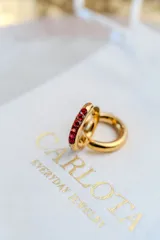 Aros tipo argolla de acero quirúrgico con baño de oro 18k, decorados con una hilera de piedras rojas engarzadas en el frente.