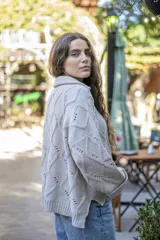 Saco tejido de punto con diseño de ochos y trenzas, color negro. Presenta cuello estilo camisero, cierre frontal con botones tipo joya, mangas holgadas y silueta oversize.