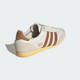 Championes Adidas modelo Japan, reedición de diseño clásico de 1964. Presentan un empeine de piel perforada en color crema con las icónicas tres bandas laterales en tono marrón. Incluyen refuerzos de gamuza en la puntera y el talón, junto con una suela de goma en tono amarillento que aporta un estilo vintage.