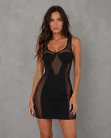 Vestido corto negro con diseño tipo corset, confeccionado con paneles de tela opaca y secciones de malla transparente en el escote y los laterales. Presenta un corte ajustado al cuerpo y escote redondo.