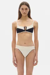 Conjunto de bikini negro con detalles en color crema. El corpiño es de corte clásico con breteles finos y abertura geométrica en el centro. La bombacha es de tiro alto con cobertura media.