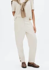 Pantalón de lino color beige, de corte recto y tiro medio, con detalle de pequeña abertura y botón en el dobladillo inferior.