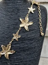 Cinto dorado de metal con eslabones y dijes en forma de estrella de mar. Incluye cadena regulable con dije esférico en el extremo.