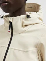 Chaqueta técnica Moncler modelo Zumeles, de color beige, con capucha ajustable, cierre frontal con cremallera termosellada y puños con detalle en contraste. Presenta un diseño entallado con bolsillos laterales y logo estampado en la manga.