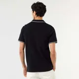 Remera polo de piqué de algodón color negro, de manga corta, con detalles de líneas blancas en el cuello y en los bordes de las mangas. Modelo EZA84.