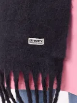 Bufanda de tejido suave con diseño de cuadros grandes en tonos naranja, rojo, violeta y lila. Presenta flecos en los extremos y una etiqueta pequeña con el logo de la marca Rusty.