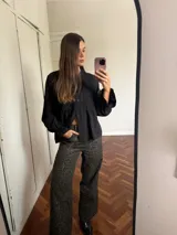 Camisa negra de corte peplum con detalles de bordado inglés en el pecho, cuello redondo y mangas largas con puños acampanados.