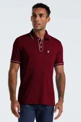 Chomba de manga corta color bordó con detalles de líneas blancas en el cuello y los puños. Presenta cierre frontal de tres botones y un bolsillo pequeño en el pecho con el logo de la marca bordado.