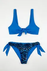 Conjunto de bikini compuesto por un top azul con nudo frontal y tirantes anchos, y una bombacha semivedetina con tiras laterales para atar y estampado animal print estilo cebra en tonos azules y negros.
