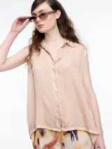 Camisa sin mangas color beige claro con efecto teñido en frío y aspecto gastado. Presenta cuello clásico, cartera oculta y ruedo irregular, más largo en los laterales.