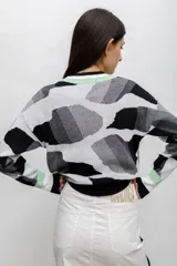 Buzo tejido en técnica jacquard con diseño de formas abstractas en tonos rojos, rosados y violetas. Presenta cuello redondo, mangas largas y puños y ruedo acanalados.