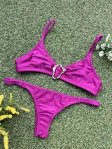 Bikini de tela metalizada color magenta, compuesto por un top con breteles finos y detalle de hebilla metálica en el centro, y una bombacha tipo colaless.