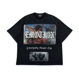Remera de manga corta color negro con efecto lavado, cuello redondo y corte holgado. Presenta estampados gráficos en el pecho, incluyendo la palabra 'EMOTION' en tipografía gótica con aplicación de brillos y la frase 'Emotions Never Die'.
