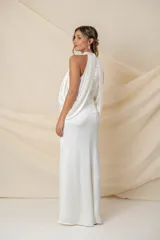 Vestido largo de novia en crepe satén de seda natural, con cuello halter y diseño drapeado que cae desde el cuello hacia la espalda.