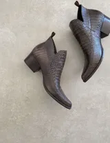 Botín corto color beige con textura símil piel de cocodrilo, taco de madera y laterales con corte en V.