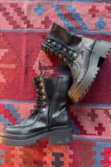 Borcego de caña corta confeccionado en cuero negro, con diseño de cordones y ganchos metálicos, cierre lateral y suela de plataforma dentada.