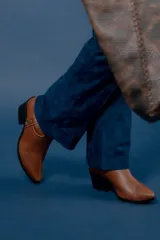 Bota de caña media color chocolate, confeccionada en cuero con textura granulada. Presenta un diseño de estilo western con punta fina, taco cuadrado y una tira lateral decorada con tachas metálicas circulares en tono bronce.