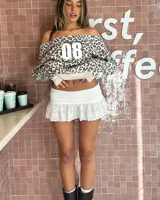 Minifalda short blanca de tiro alto, con cintura fruncida y vuelo inferior con detalles de bordado inglés y encaje calado.