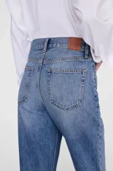 Pantalón jean de tiro alto y pierna recta amplia, color azul medio con efecto lavado. Presenta detalles de roturas sutiles a la altura de las rodillas y diseño clásico de cinco bolsillos.