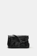 Bolso de hombro color negro con acabado efecto cuero desgastado, solapa frontal y detalle de cadena metálica oscura. Cuenta con tres compartimentos internos, uno de ellos con cierre de cremallera, y cierre principal mediante imán.