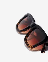 Lentes de sol unisex Hawkers modelo One Uptown, con montura cuadrada de acetato color negro y carey, y lentes degradadas color marrón.