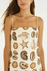 Vestido largo con estampado de caracoles y estrellas de mar, escote recto y tirantes finos. Cuerpo de algodón con forro y falda plisada de tejido liviano semitraslúcido.