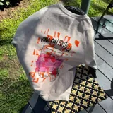 Buzo de cuello redondo en color crema, con diseño estampado en la espalda que incluye un gráfico de una copa con frutillas y la frase 'Vino con frutilla'.