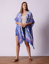Kimono tejido con estampado abstracto en tonos azules, blancos y violetas. Tiene terminación de ruedo con borlas.