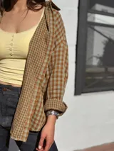 Camisa escocesa holgada, de manga larga, con estampa de cuadros en tonos de verde y marrón, y cierre frontal con botones.