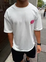 Remera blanca de corte oversize, confeccionada en algodón, con cuello redondo y una pequeña estampa de un helado de palito color rosa en el pecho.