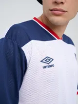 Remera de fútbol Umbro del Club Nacional de Football, de diseño tricolor con cuerpo azul marino, mangas y canesú rojos, y cuello en V con detalles en blanco y azul. Incluye el logo de Umbro en el pecho derecho y el escudo del club en el izquierdo.