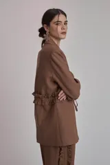 Blazer negro con solapas de muesca, corte holgado, cierre frontal con lazo y detalle de volados en los bolsillos.